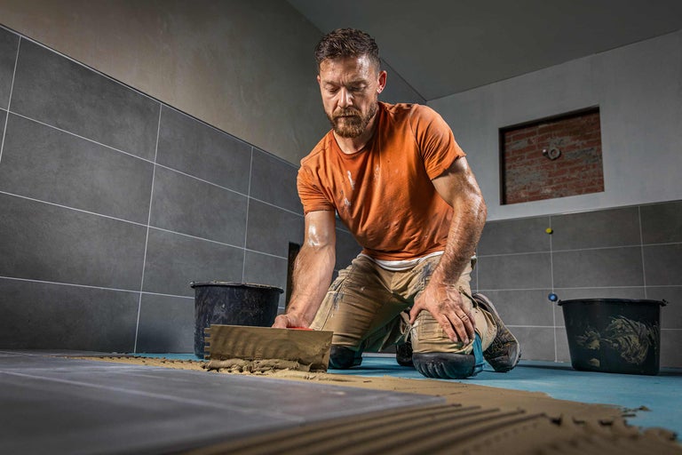 Carreleur au travail: Pose de carreaux avec une spatule et un seau dans une salle de bains.