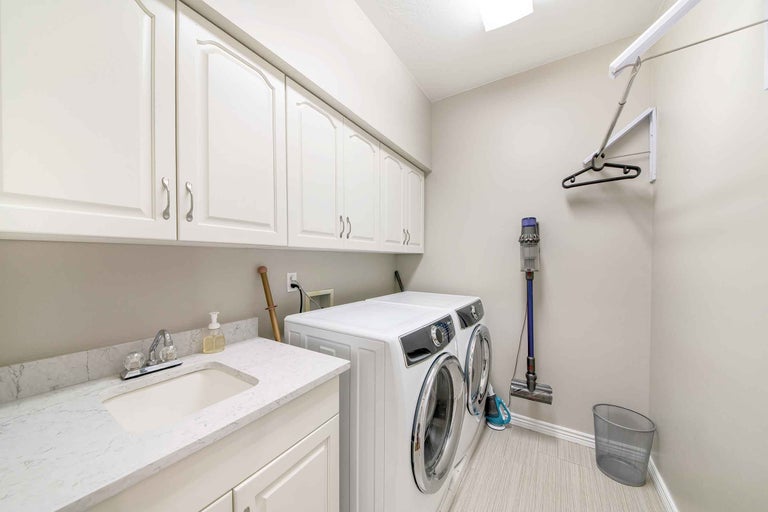 Buanderie avec lave-linge, sèche-linge, évier, placards et aspirateur