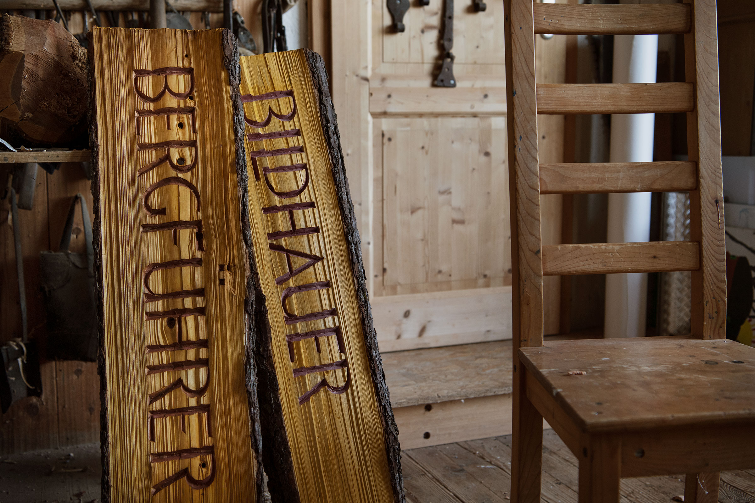 Zwei Holzschilder mit den Aufschriften Bergfuehrer und Bildhauer neben einem Holzstuhl.