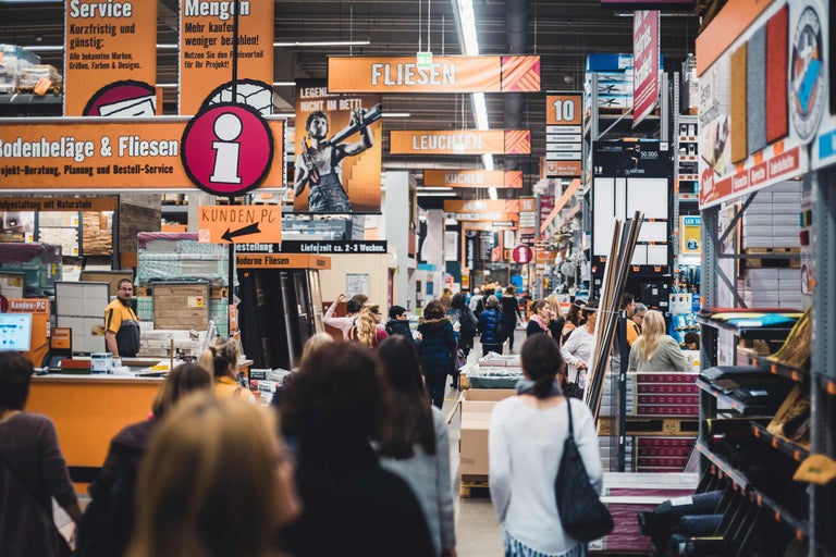 Vue intérieure d'un magasin de bricolage Hornbach avec des clients et des panneaux indiquant différents rayons tels que le carrelage et les luminaires
