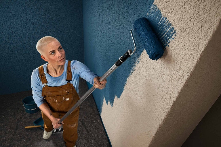 Eine Person streicht eine Wand mit einer Farbwalze.