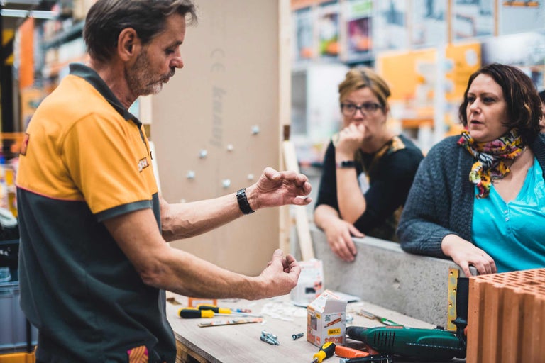 Un artisan explique à deux clientes différents outils et matériaux de construction dans la quincaillerie Hornbach.