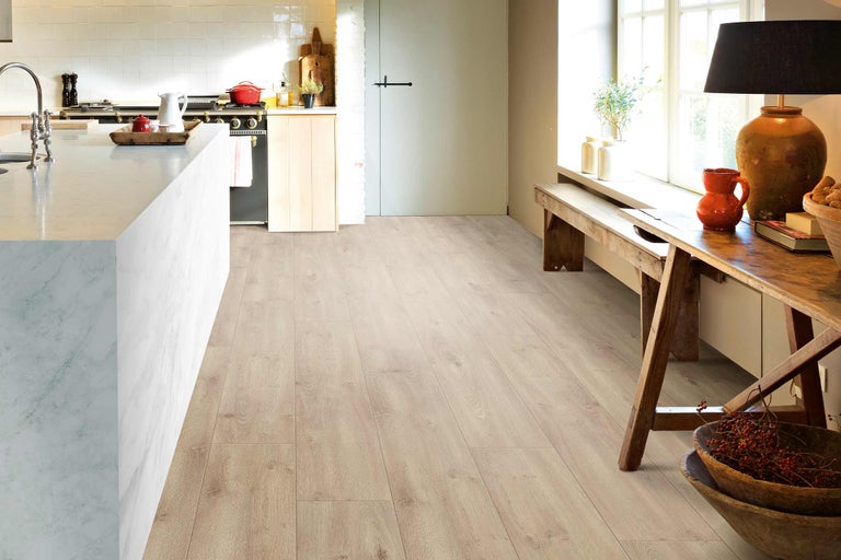 Cuisine claire avec sol stratifié imitation bois, îlot de cuisine et coin salon près de la fenêtre.