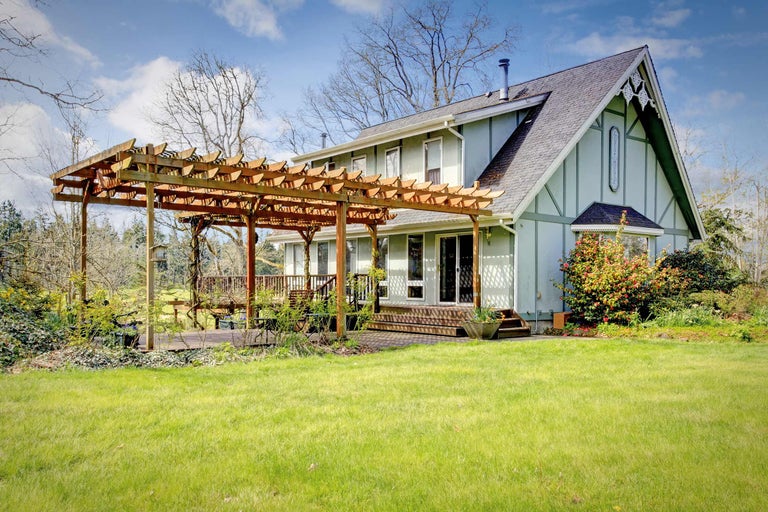 Une maison avec une pergola en bois, une terrasse et une pelouse.