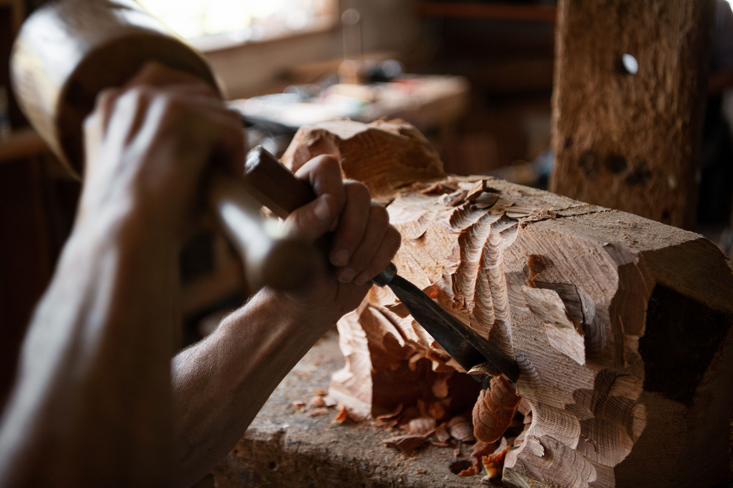 Ein Mann benutzt einen Holzhammer und ein Stecheisen, um ein Stück Holz zu bearbeiten.