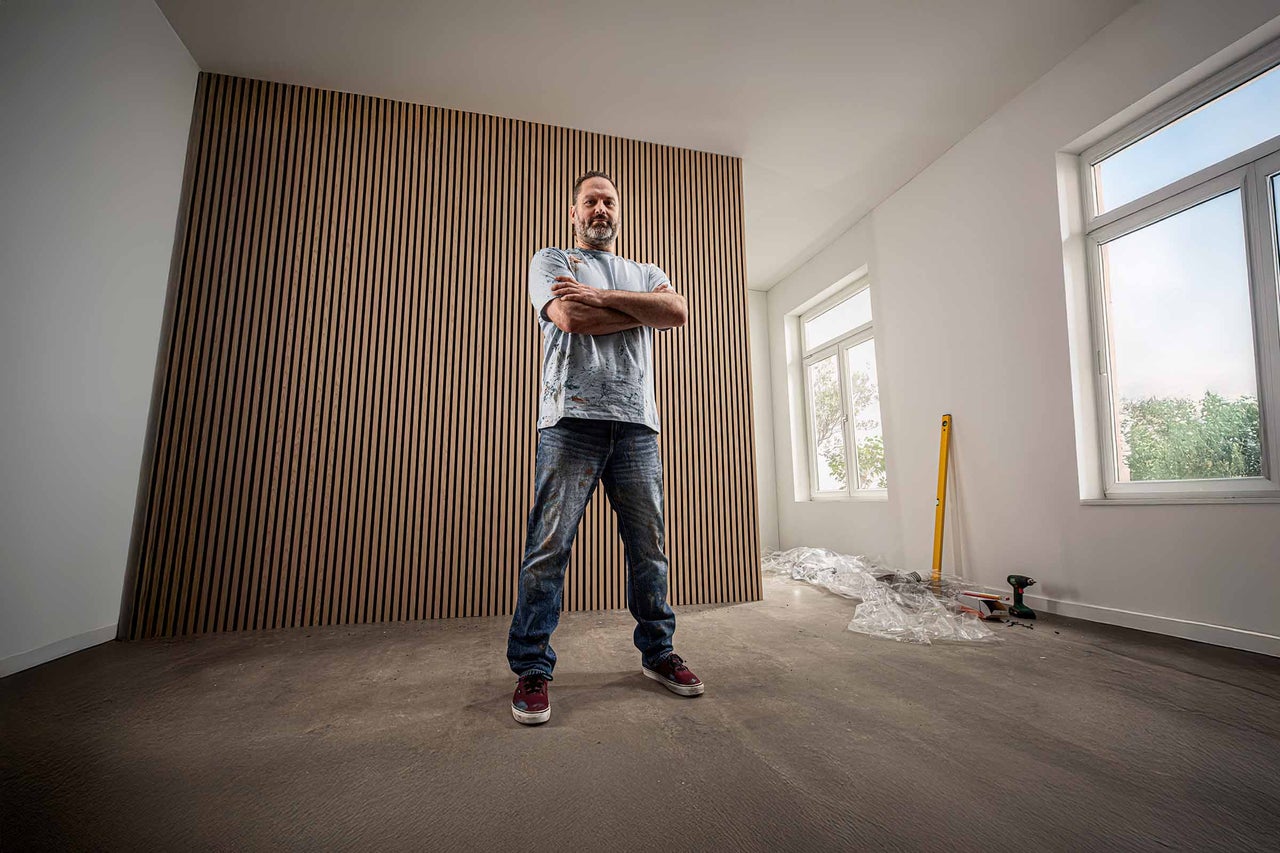 Mann steht vor einer Wandverkleidung aus Holzlatten in einem hellen Raum.