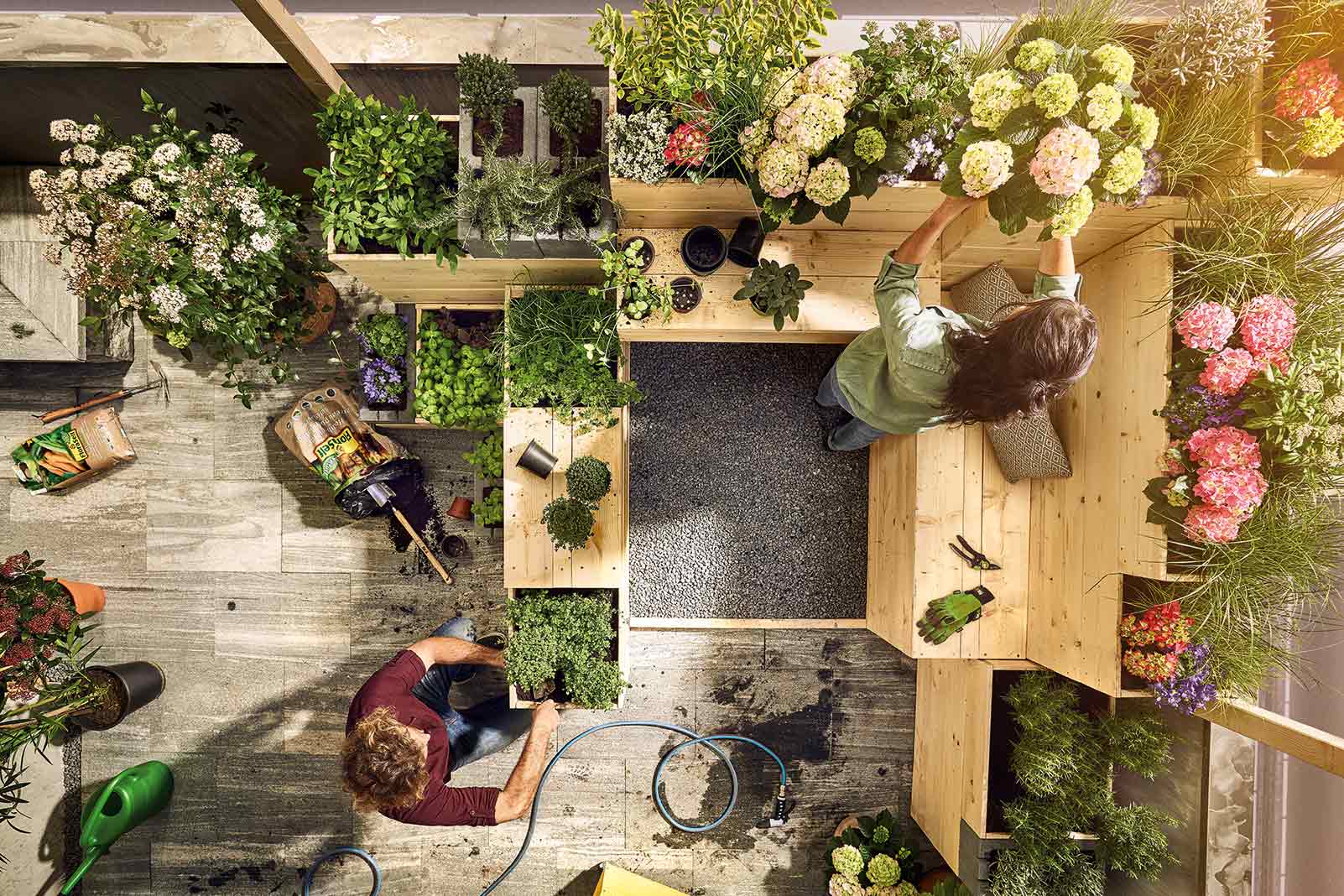 Dachterrassen-Szene mit Personen, Pflanzen in Holzkästen, Gartengeräten und Bewässerungsschlauch