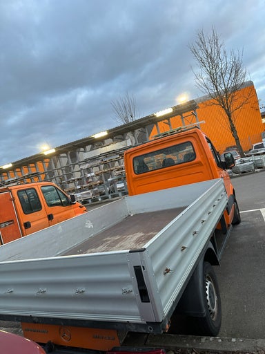 Foto eines orangefarbenen Pritschenwagens auf einem Parkplatz vor einem Hornbach Baumarkt.