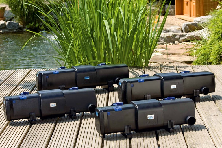 Mehrere Oase Bitron Teichklärer auf Holzdeck mit Teich im Hintergrund.