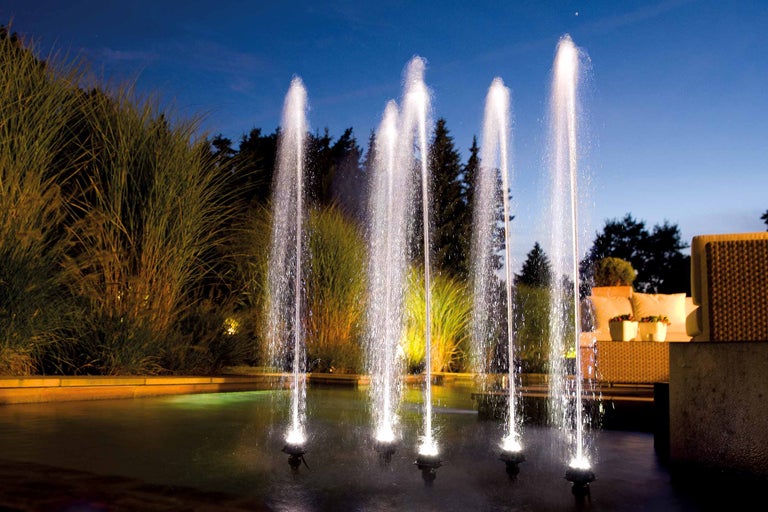 Gartenbrunnen mit mehreren Fontänen im abendlichen Garten