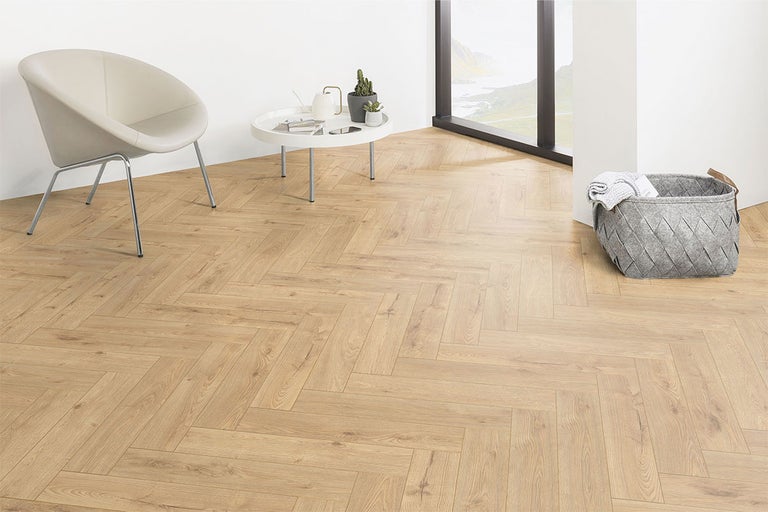 Pièce claire avec parquet à chevrons, fauteuil, table et panier