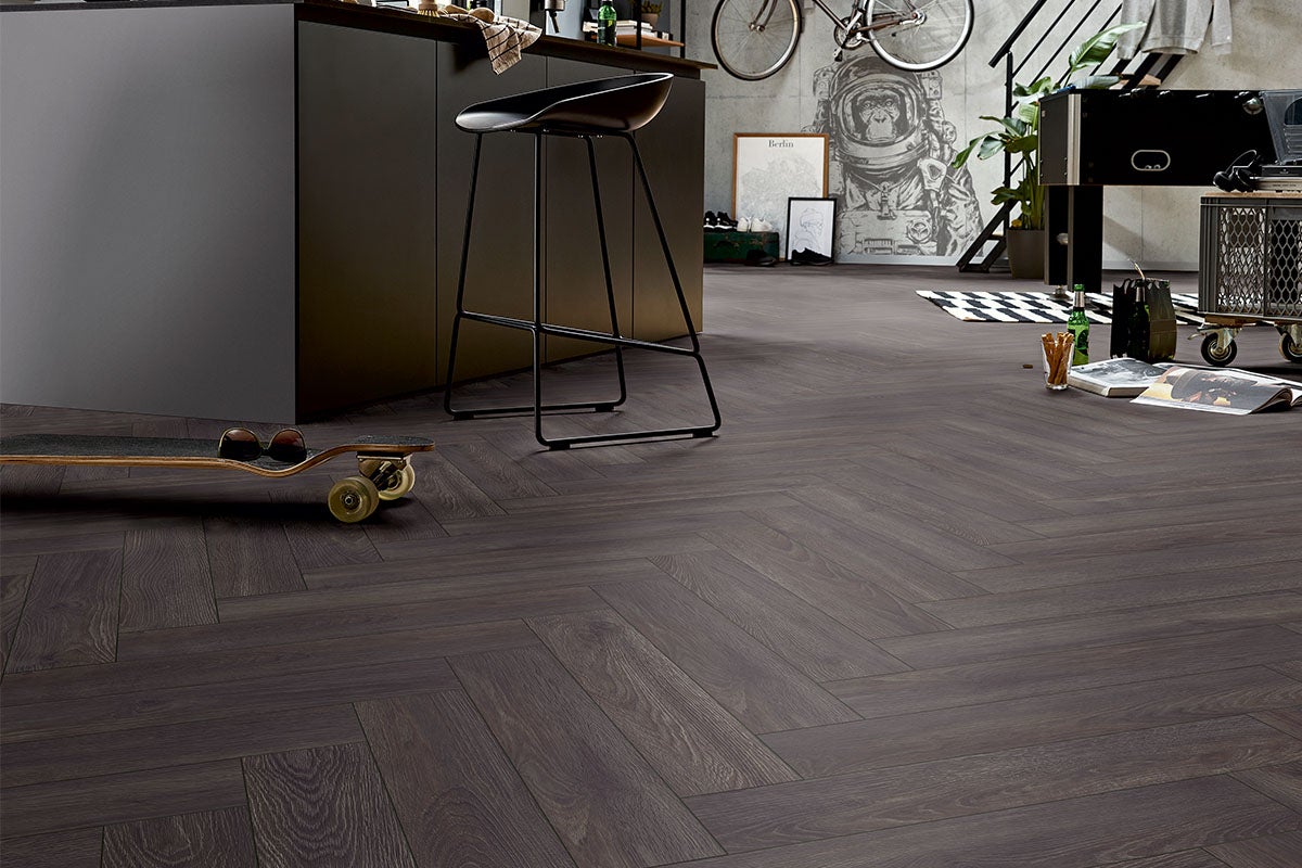 Intérieur avec plancher en bois foncé à chevrons, complété par un îlot de cuisine, un tabouret de bar et des éléments décoratifs