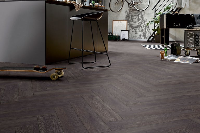 Intérieur avec plancher en bois foncé à chevrons, complété par un îlot de cuisine, un tabouret de bar et des éléments décoratifs