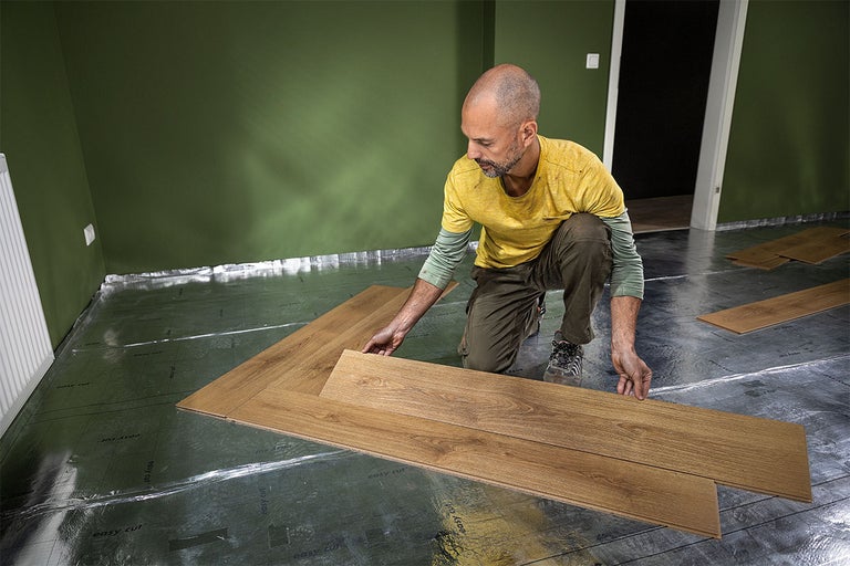 Un homme pose du stratifié sur une couche d'isolation dans une pièce.
