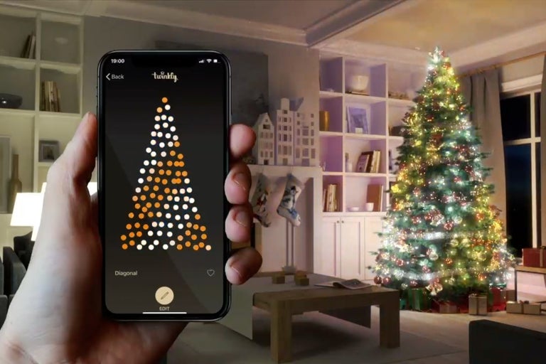 Handy mit Twinkly App zur Steuerung einer Lichterkette an einem Weihnachtsbaum im Wohnzimmer