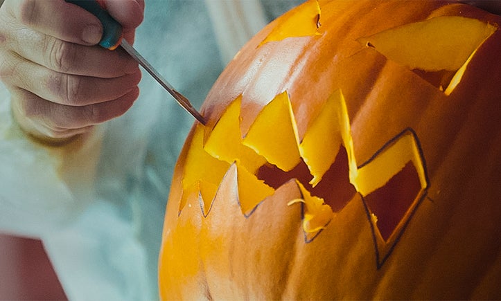 Une personne sculpte une citrouille d'Halloween avec un outil.