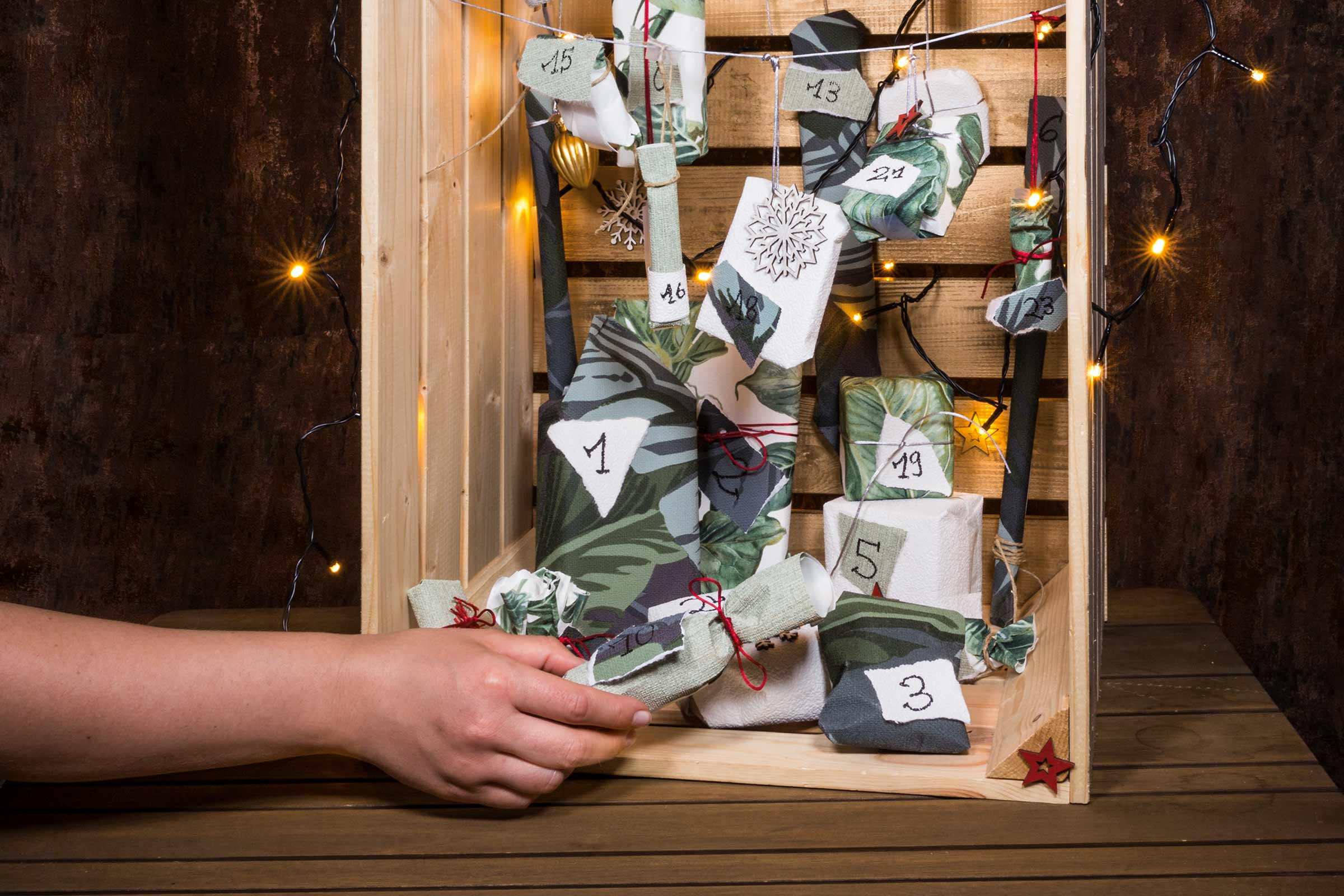 Une main prend un sachet dans un calendrier de l'Avent dans une boîte en bois
