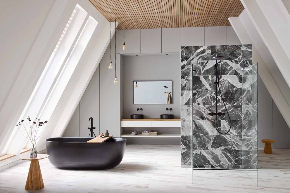 Salle de bain lumineuse avec pentes de toit, baignoire noire, meuble-lavabo avec deux lavabos, espace douche avec carreaux de marbre et éléments en bois