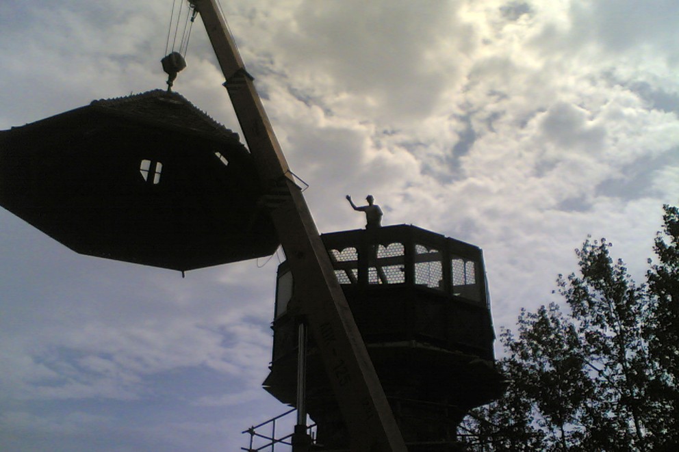 
				Der Burgherr dirigiert im Gegenlicht: Das Holzdach des großen Burgturms wird mit dem Mobilkran auf den Turm gesetzt.

			