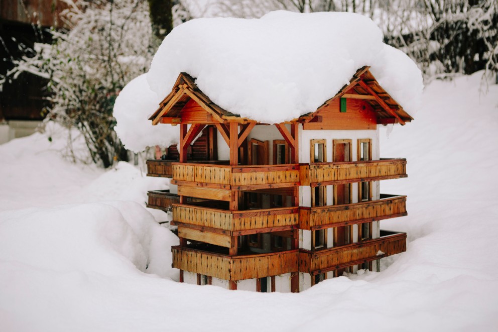 
				Bauernhausmodell im Garten, halb versunken im Neuschnee.

			