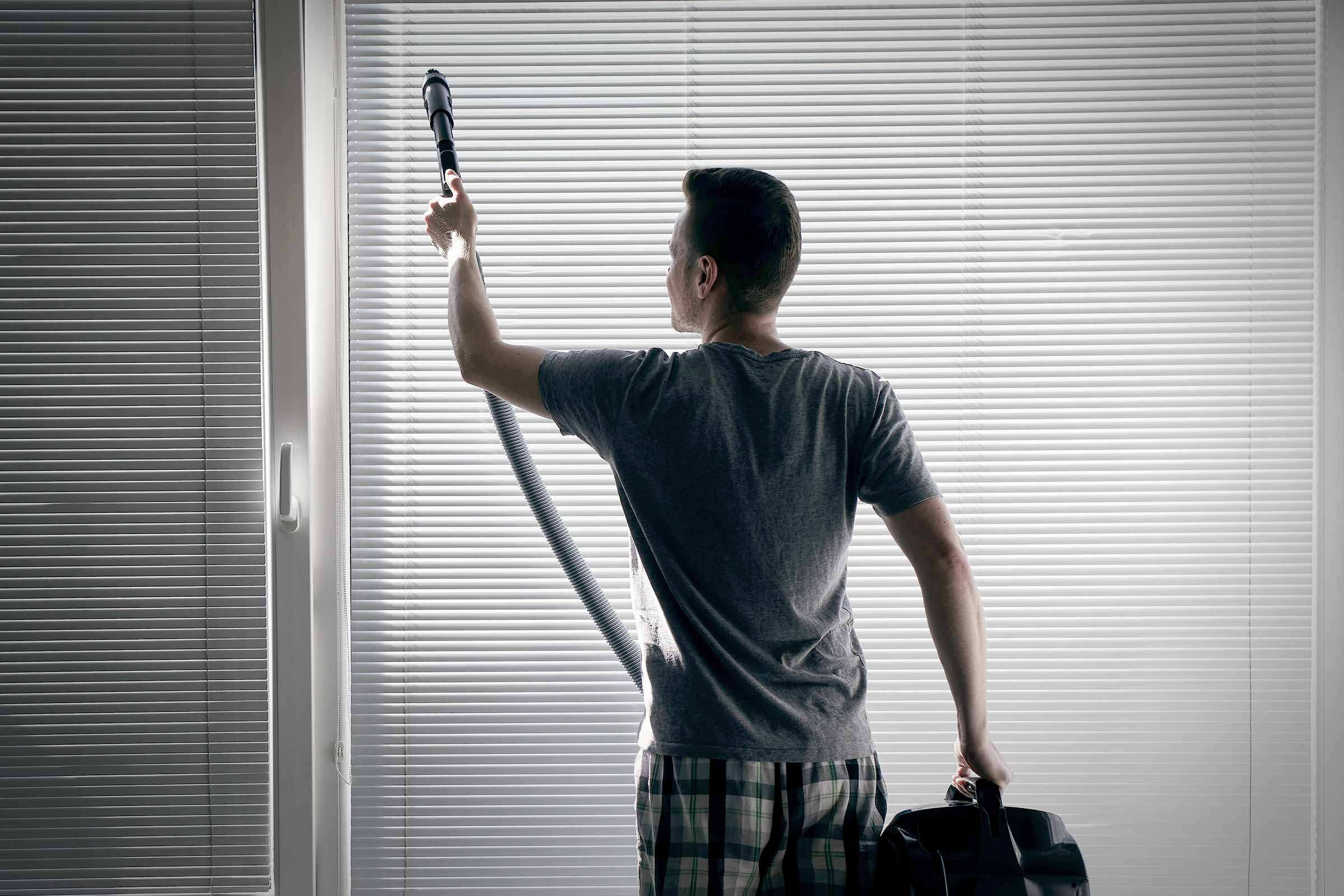 Un homme nettoie les stores avec un aspirateur