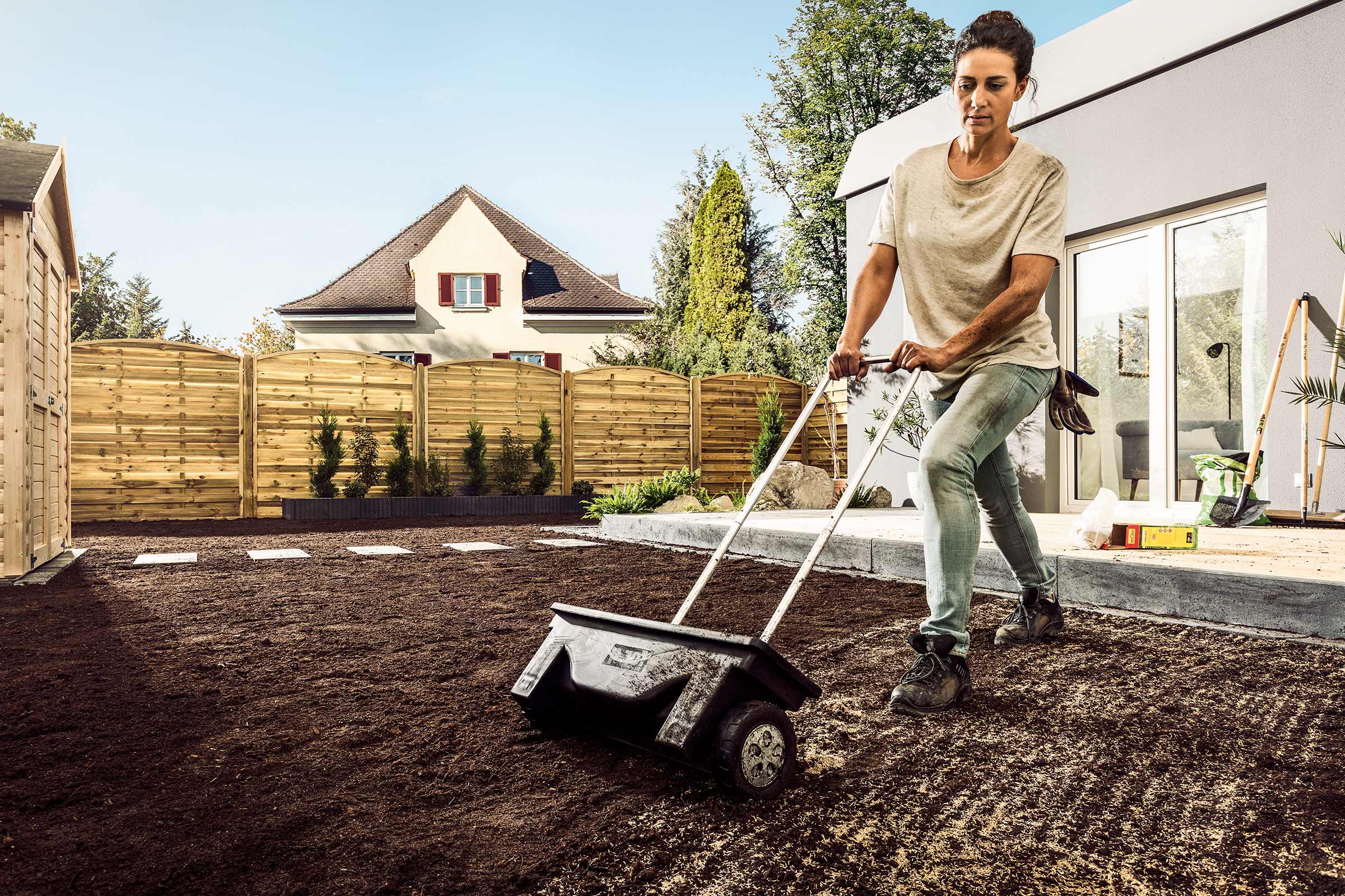 Une femme utilise un épandeur pour répartir les graines de gazon dans le jardin.
