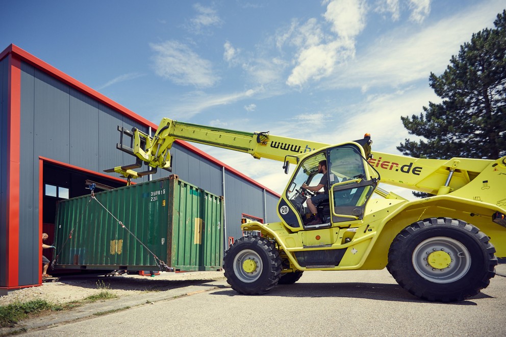 
				Kunststück mit Kran. Weil der Kran nicht durchs Tor passt, werden innen unter die Container selbst gebaute Rollwagen untergeschoben.

			