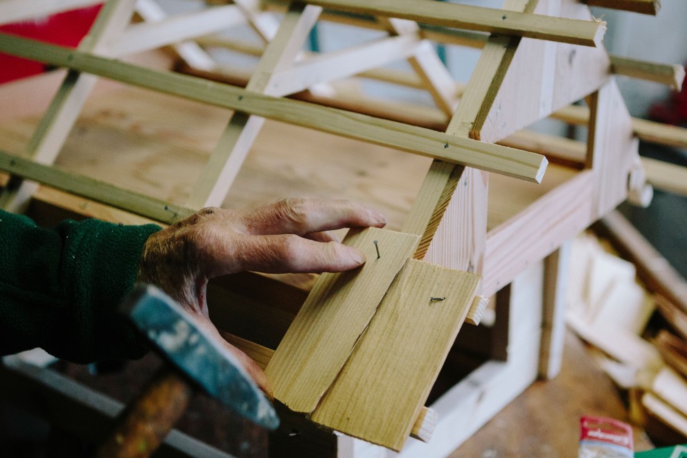 
				Mann befestigt mit einem Nagel eine Schindel aus Holz am Modell.

			