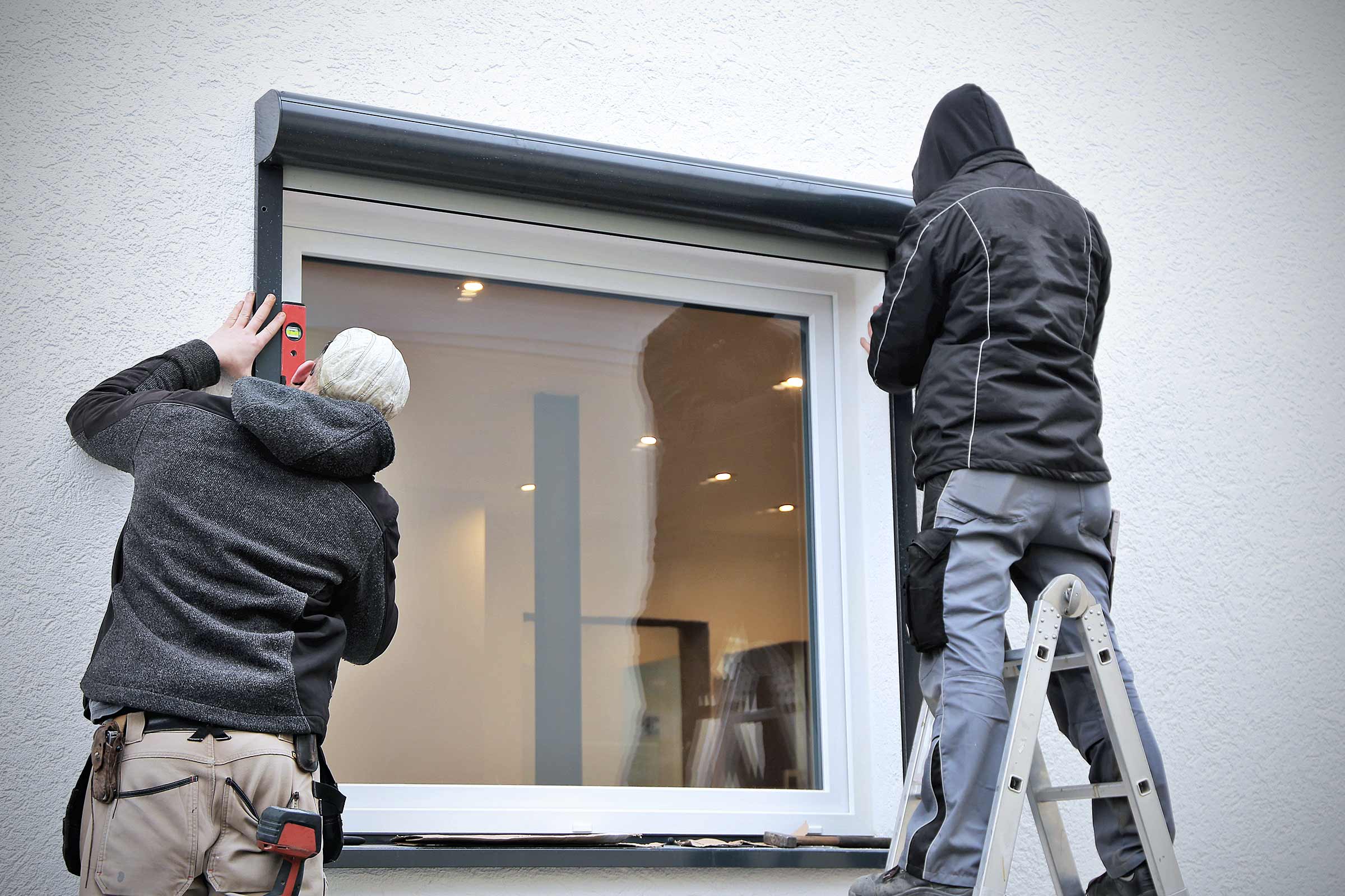 Deux installateurs installent un volet roulant sur une fenêtre.