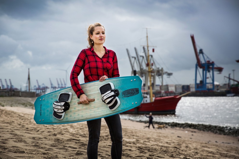 Autorin Esther Acason steht mit dem selbst gebauten Kiteboard unterm Arm am Hamburger Elbstrand