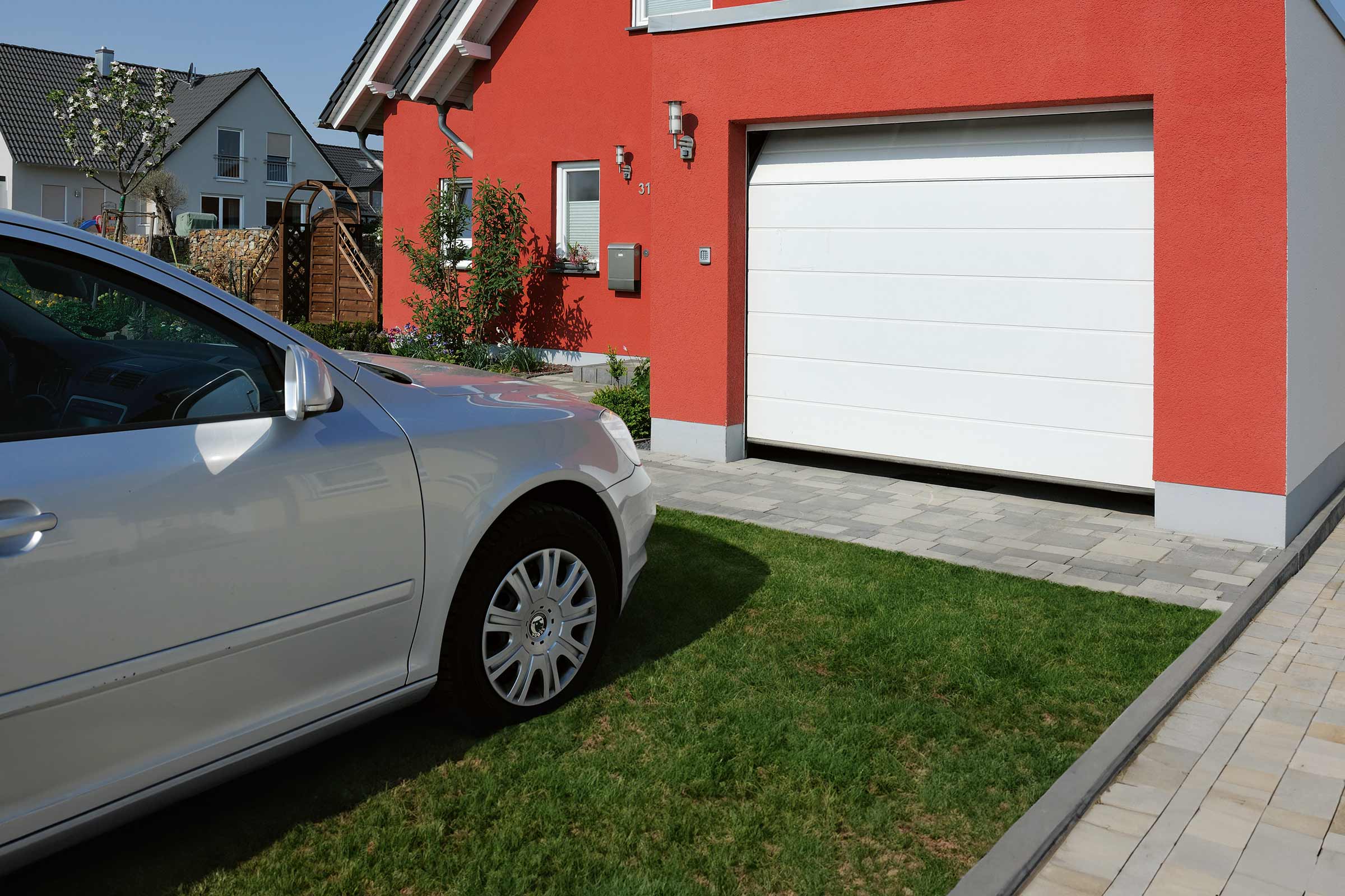 Une maison individuelle avec une porte de garage blanche, une façade rouge et une allée pavée avec une pelouse.