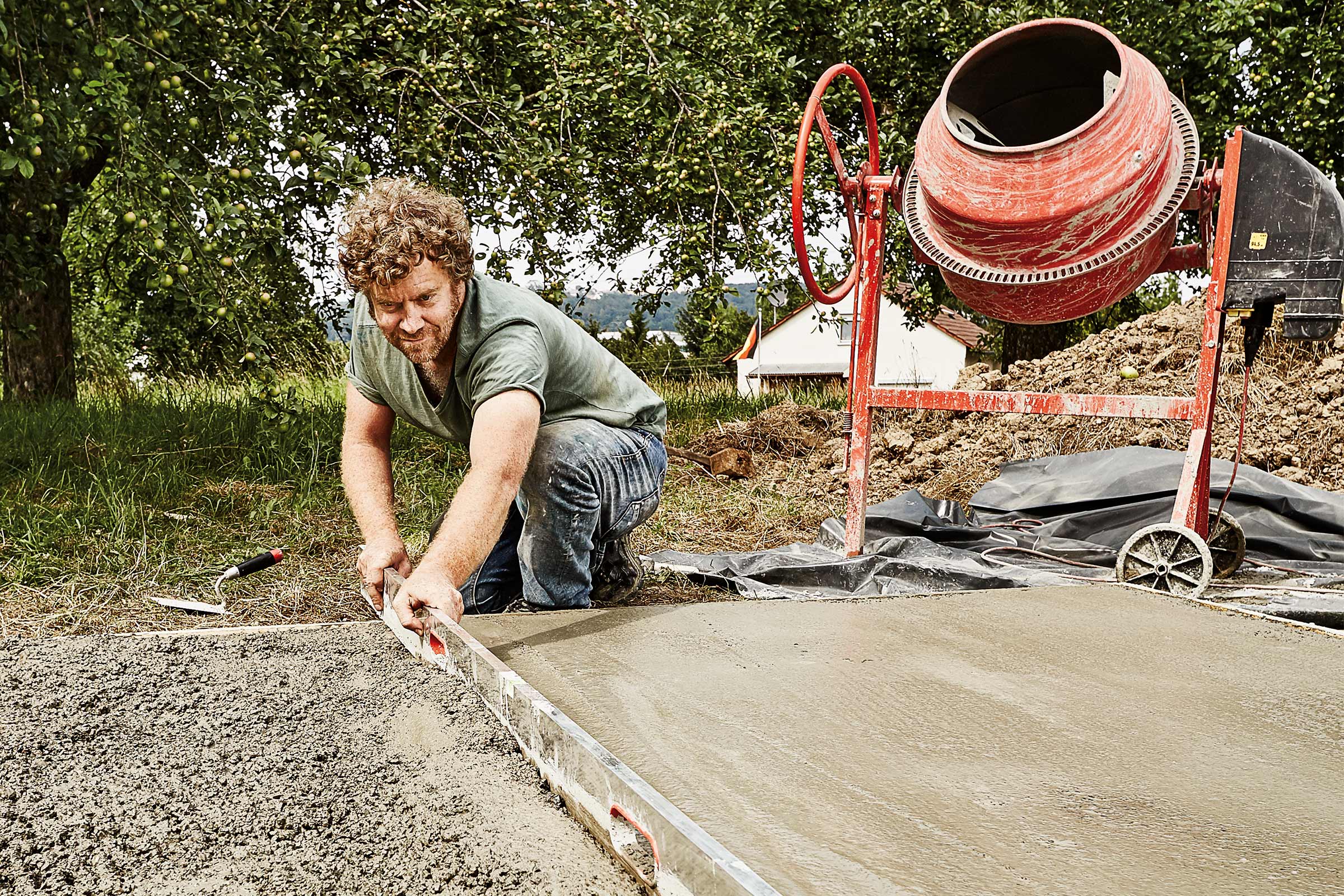 Un homme lisse le béton à la règle près d'une bétonnière