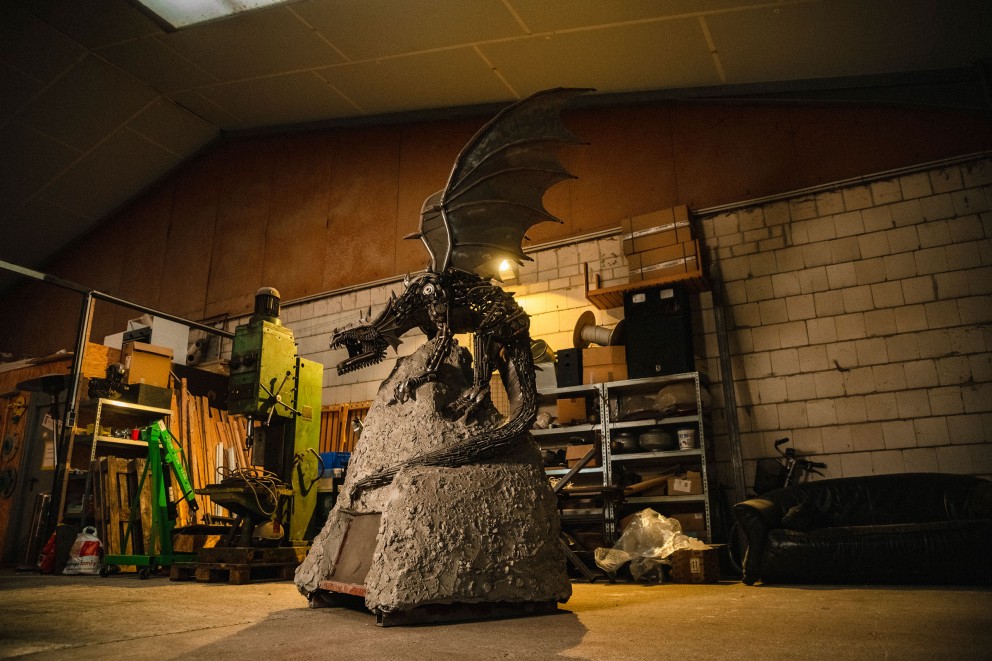Ein Drache aus Schrott Teilen auf einem Betonsockel in einer Werkstatthalle. Ein Drache aus Schrott Teilen auf einem Betonsockel in einer Werkstatthalle.