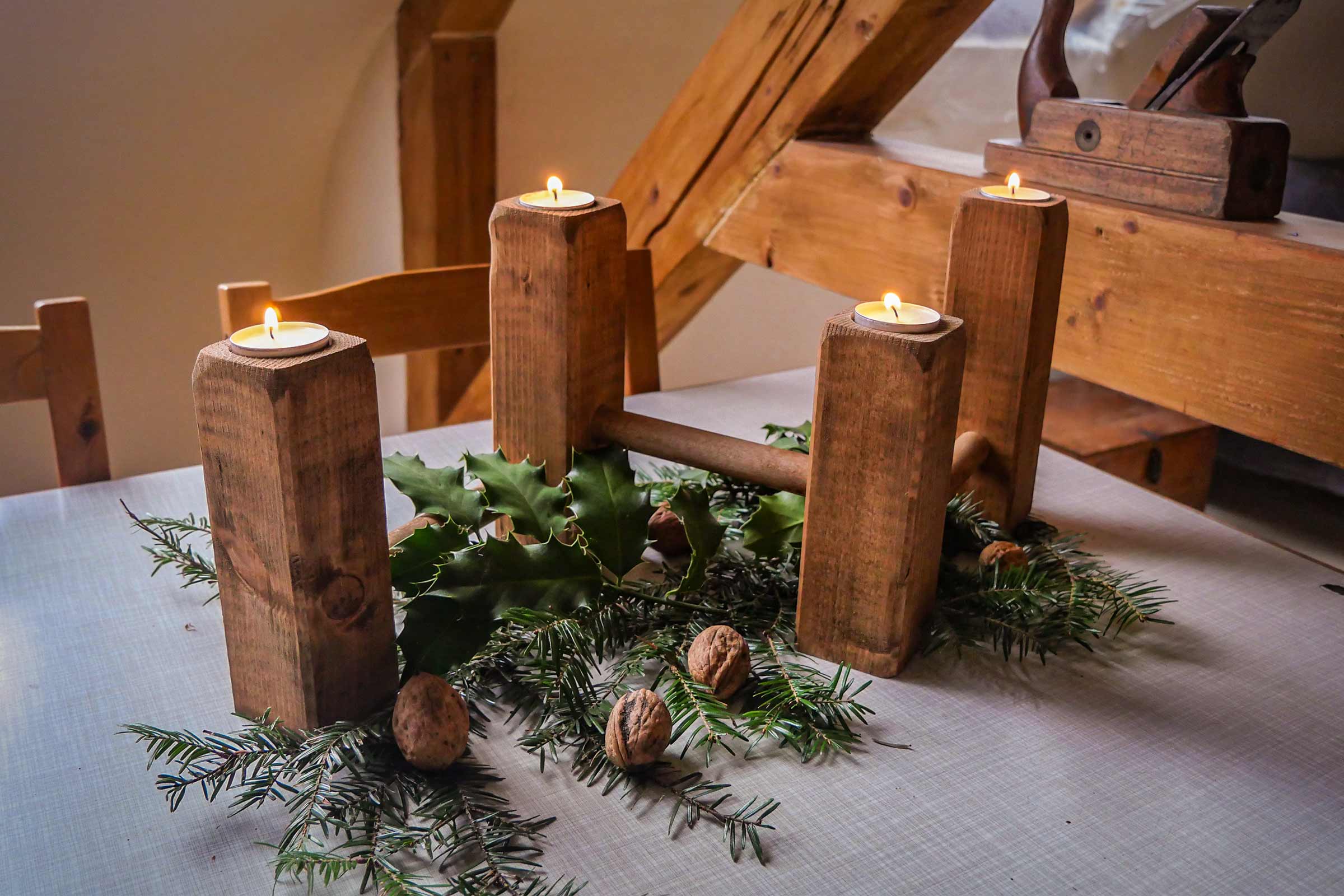 Couronne de l'Avent avec quatre bougies chauffe-plat, branches de sapin, noix et feuilles de houx sur une table