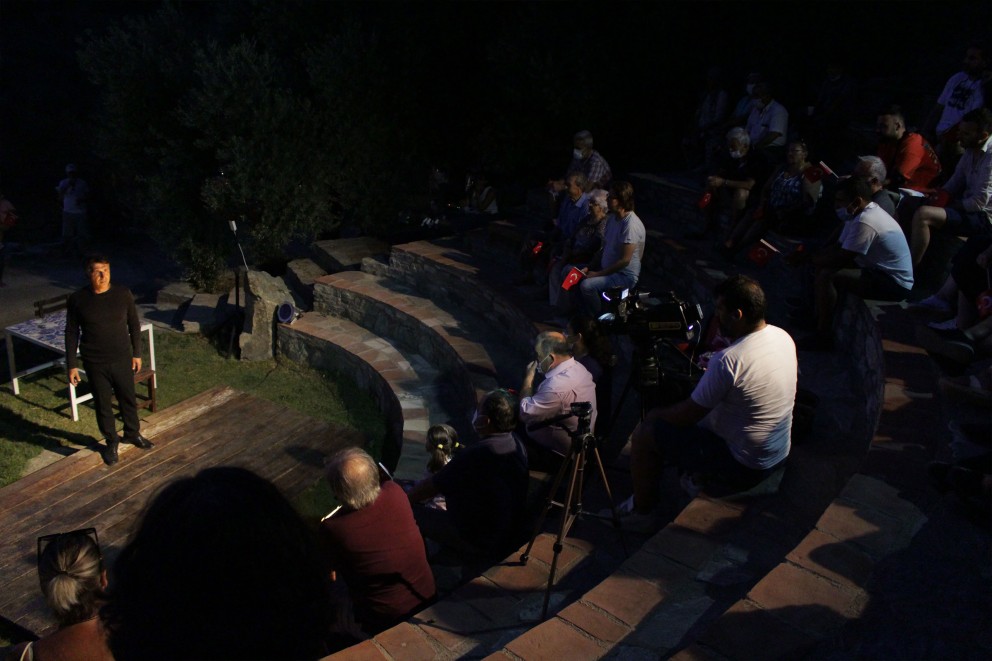 
				Schauspieler auf Holzbühne in antikem Amphitheater.

			