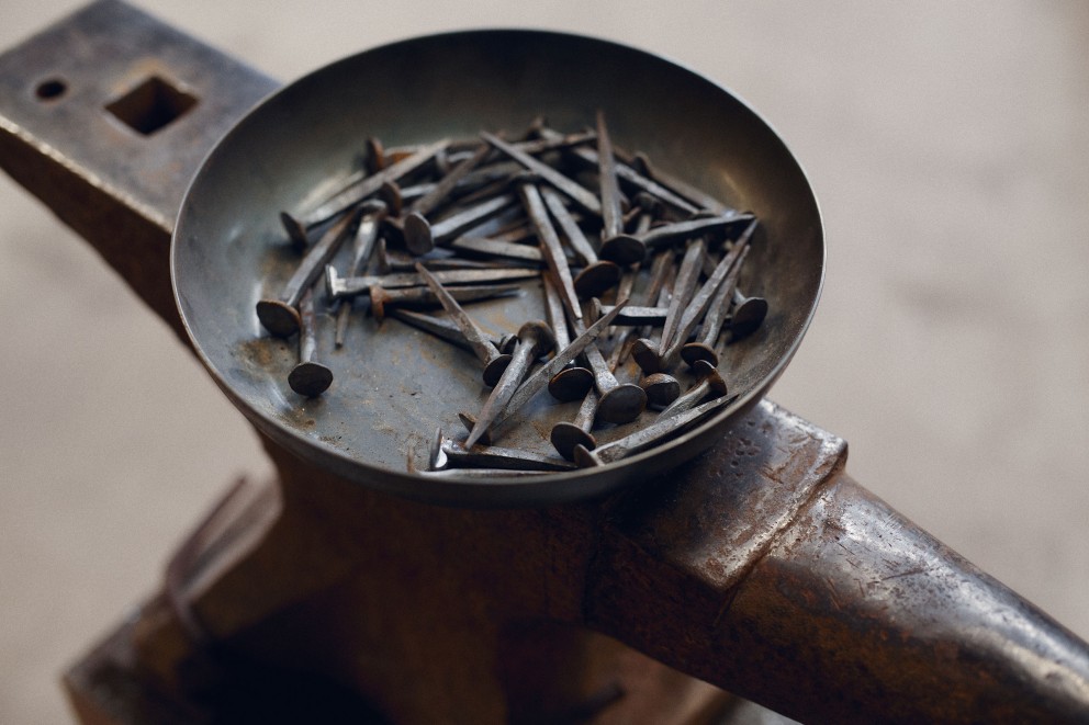 Auf einem Amboss steht eine Metallschale mit schwarzen Nägeln aus Stahl. Auf einem Amboss steht eine Metallschale mit schwarzen Nägeln aus Stahl.