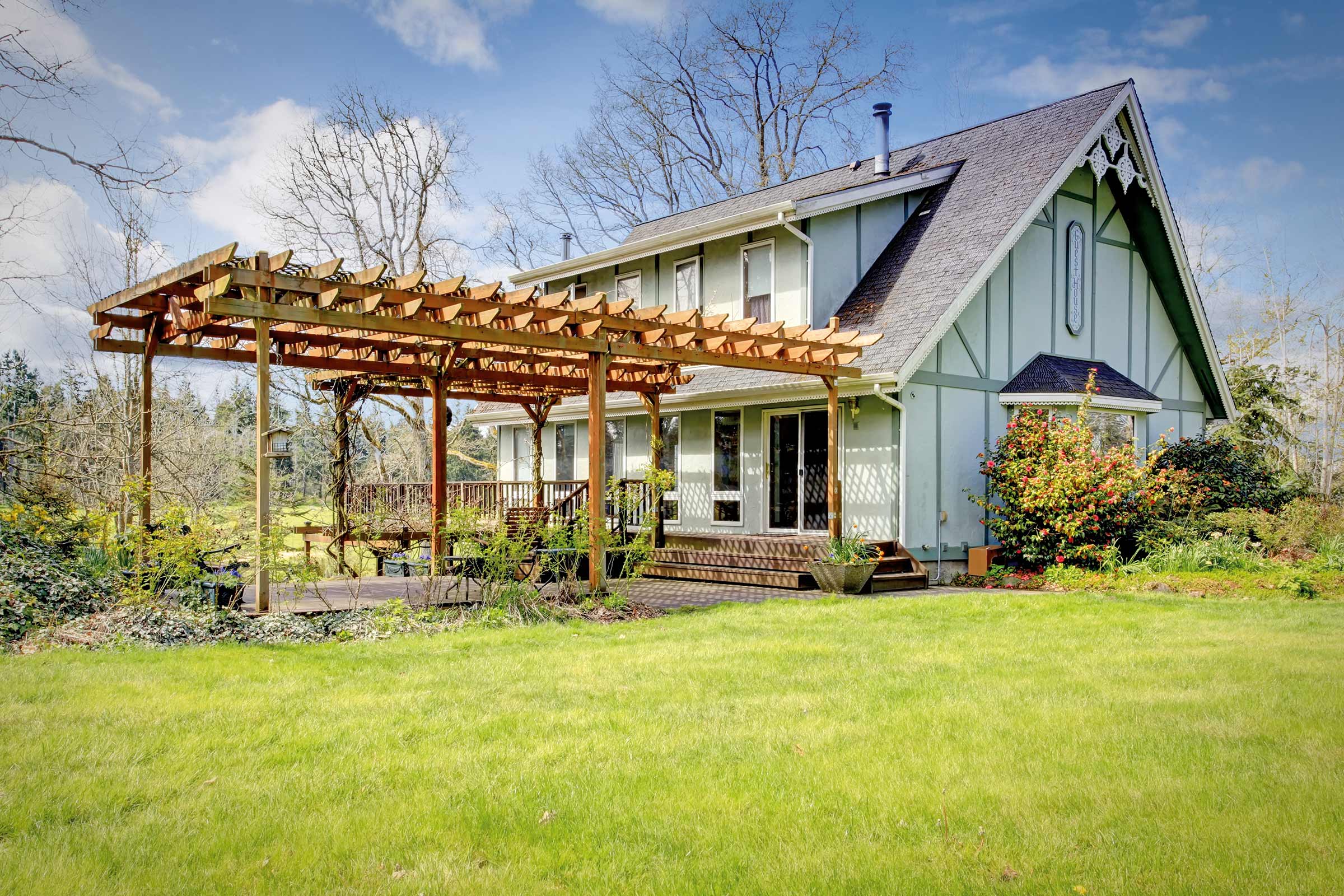 Une maison avec une pergola en bois, une terrasse et une pelouse.