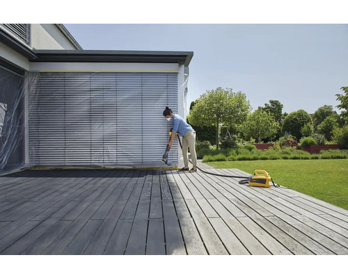 Une femme vaporise une terrasse en bois avec un système de pulvérisation de peinture
