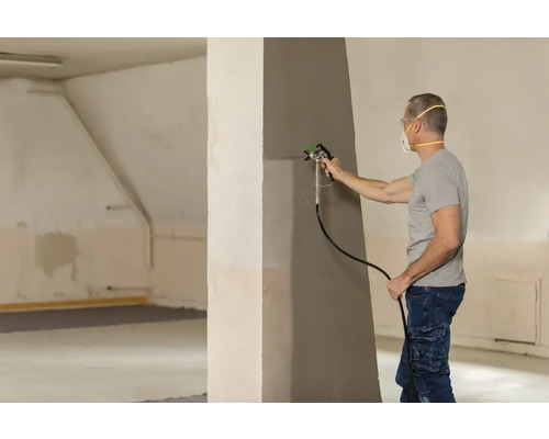 Homme peint un mur avec un pulvérisateur de peinture