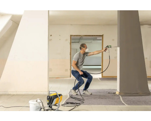 Un homme utilise un pulvérisateur de peinture dans une pièce pour peindre un pilier