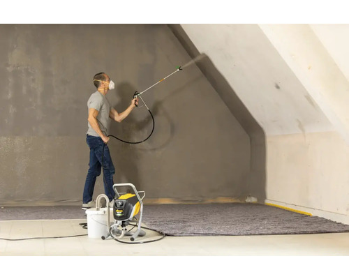 Un homme pulvérise de la peinture avec un pulvérisateur de peinture sur un mur dans une pièce.