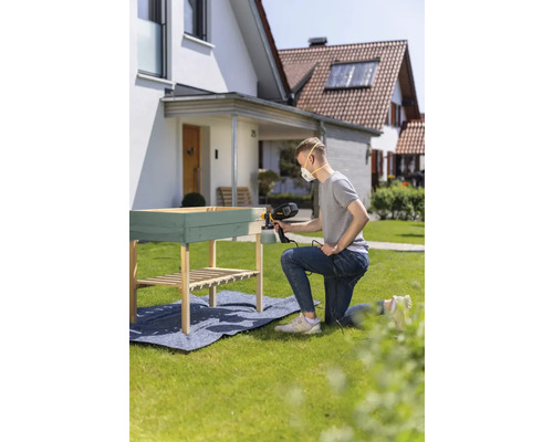 Un homme pulvérise une table en bois dans le jardin avec un pulvérisateur de peinture.