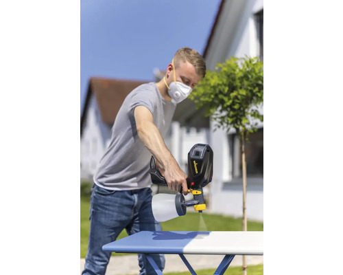 Un homme utilise un pulvérisateur de peinture pour peindre une table à l''extérieur.