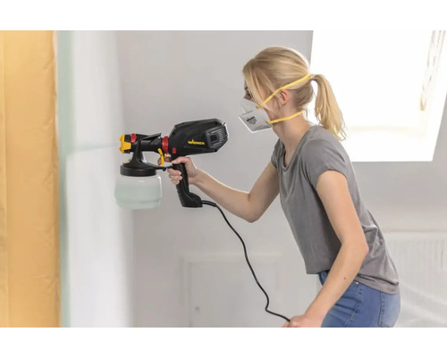 Une femme vaporise de la peinture sur un mur avec un pistolet à peinture.