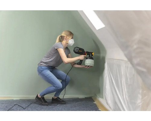 Une femme utilise un pulvérisateur de peinture dans une pièce recouverte de film plastique.