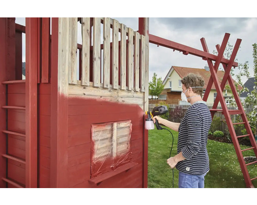 Une personne vaporise une maison de jeu en bois avec un pistolet à peinture