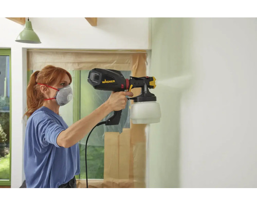 Femme peint un mur avec un système de pulvérisation de peinture Wagner