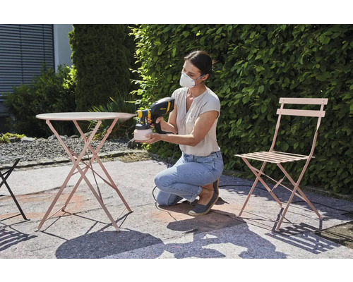 Femme peignant une table de jardin et une chaise avec un système de pulvérisation de peinture