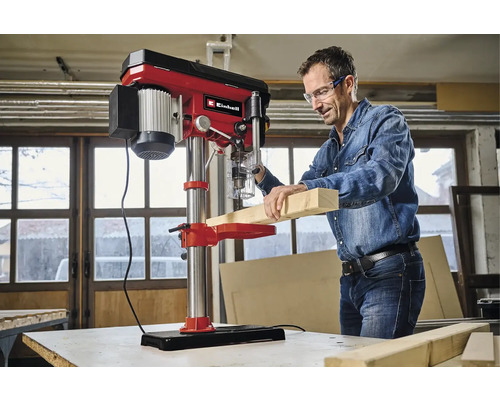 Ein Mann bohrt mit einer Tischbohrmaschine ein Holzbrett.