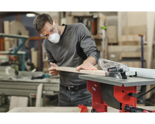 Un homme coupe une planche de bois avec une scie circulaire de table Einhell dans un atelier.